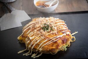 The Hiroshima-style okonomiyaki layers each of the ingredients onto the pancake whereas the Osaka-style okonomiyaki mixes all of the ingredients together