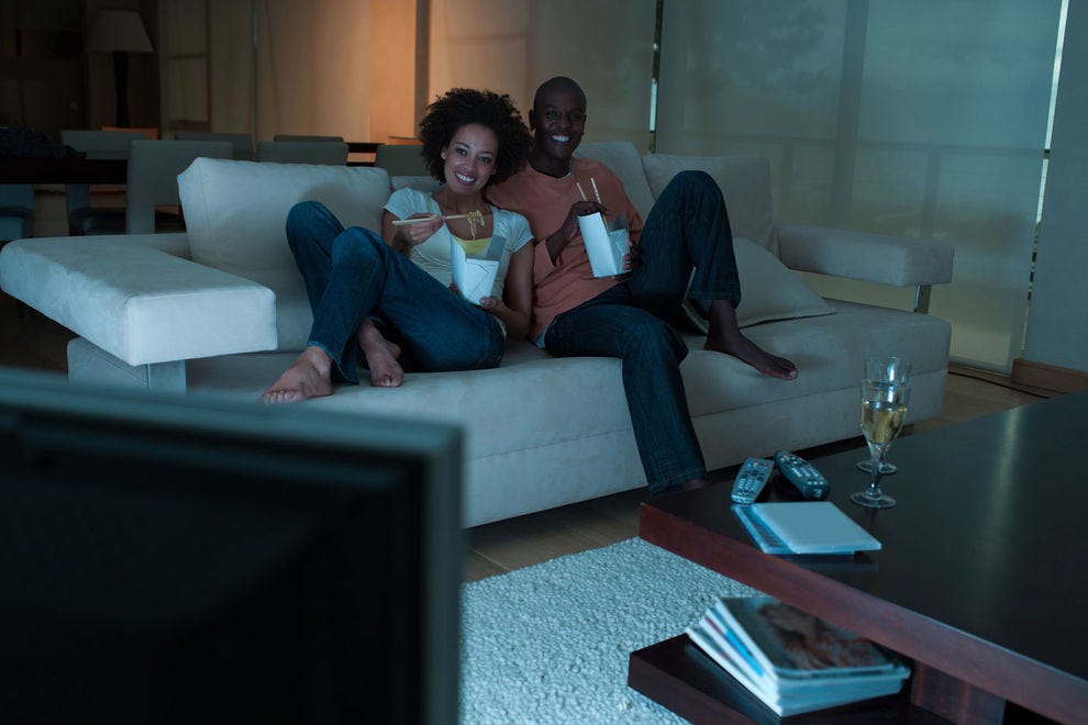 Couple devant la télé et manger de la nourriture sur le canapé