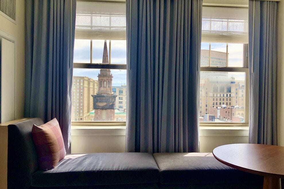 Un lit de repos en velours gris dans une chambre avec vue sur la ville donne sur l'église de la rue Arlington